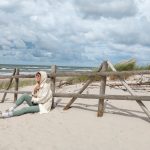 Person in casual attire sits on Baltic beach, enjoying the serene sea view.
